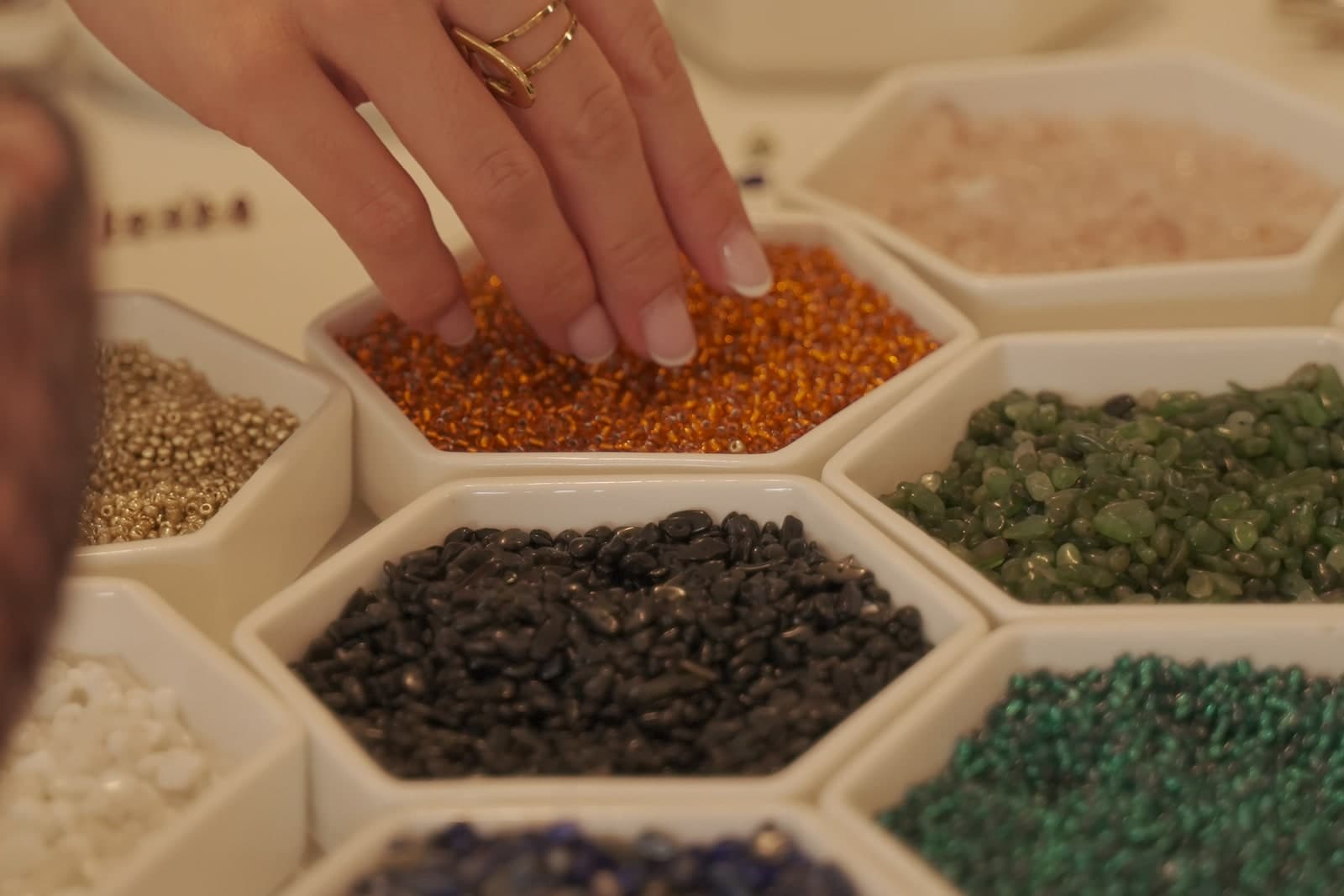 Una mano elige cuentas de colores entre recipientes de materiales