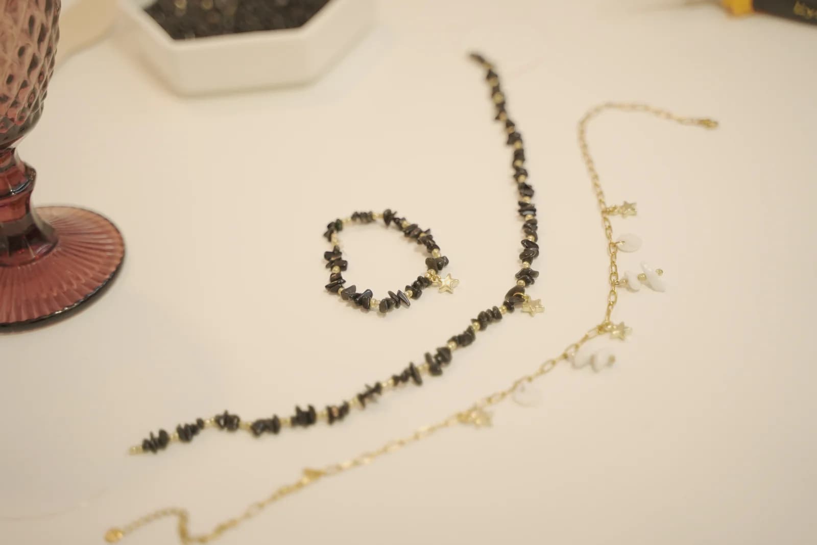 Collar de cuentas oscuras, pulsera y collar de cadena con charms sobre una mesa.