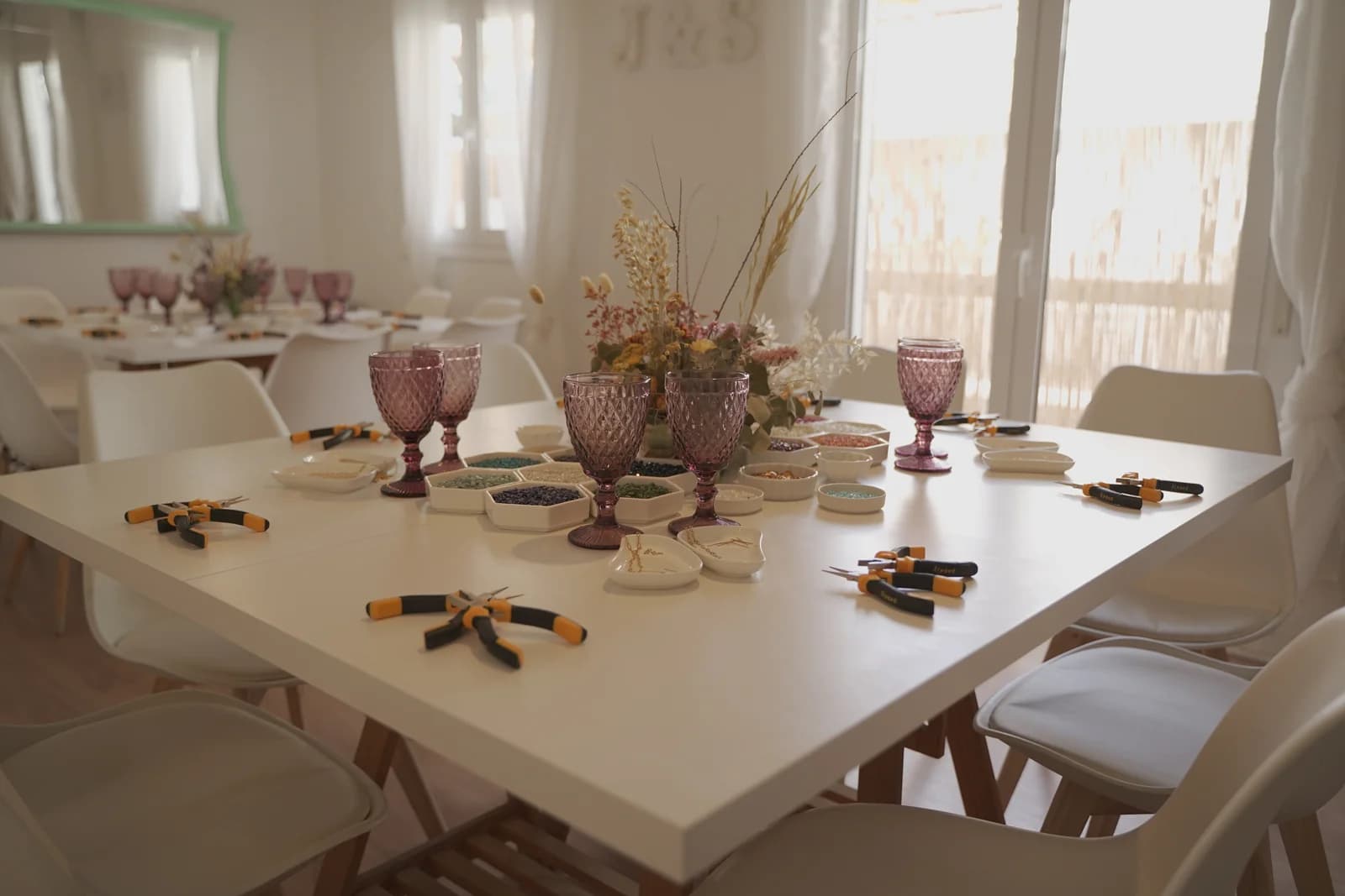 Mesa del taller preparada con alicates, cuentas, copas y bandejas para joyas.